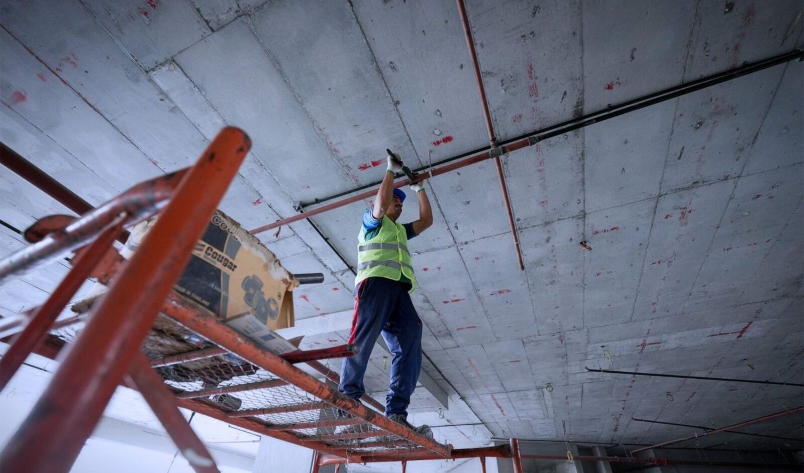 Un technicien sur un échafaudage roulant intervient sur des réseaux en plafond