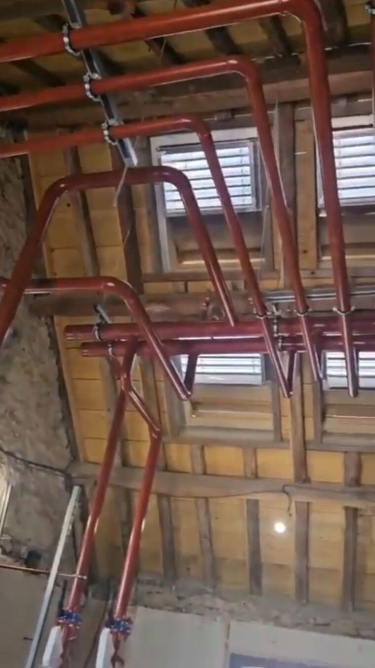 Réseau de tuyauterie rouge posé sous une charpente bois